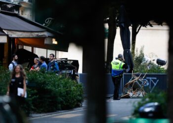 Security stand next a damaged vehicle near the bar "Le Ramus" where a motorist drove onto the terrace of a cafe, leaving several injured, in Paris on July 17, 2024. - A police source told AFP that the investigation into the car that ploughed into the terrace of a bar in Paris on July 17, killing one and injuring six people, is currently focusing on a road accident. (Photo by IAN LANGSDON / AFP)