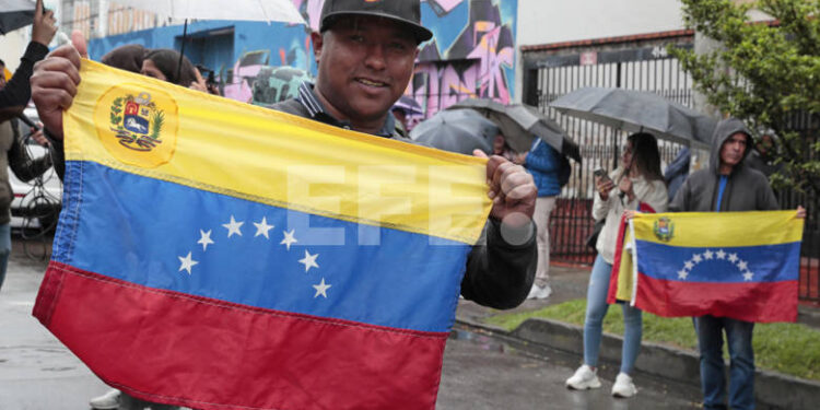 AME5600. BOGOTÁ (COLOMBIA), 28/07/2024.- Ciudadanos venezolanas posan con la bandera de su país frente al puesto de votación en las elecciones presidenciales de Venezuela este domingo, en Bogotá (Colombia). "Esperamos que se cumpla con la con la ley, que se cumple con el mandato de los ciudadanos y que se cumpla con la democracia", explicó emocionado a EFE Álvaro Carranque, uno de los primeros venezolanos que depositó su voto en Bogotá en los comicios presidenciales de este domingo. EFE/ Carlos Ortega