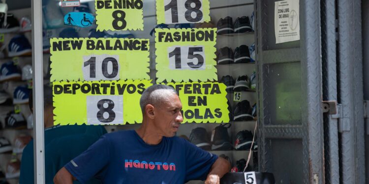 AME464. CARACAS (VENEZUELA), 09/07/2024.- Un hombre espera afuera de una tienda de zapatos donde se ven los precios, el 8 de julio de 2024, en Caracas (Venezuela). La inflación en Venezuela, que en junio cayó hasta el 1 %, se ha desacelerado a raíz de una política para estabilizar el precio del dólar -divisa usada en el país para cotizar bienes y servicios-, para lo que también se han "sacrificado" salarios y créditos bancarios, advierten expertos. EFE/ Ronald Peña