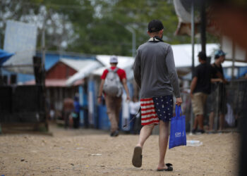 ACOMPAÑA CRÓNICA: PANAMÁ CRISIS MIGRATORIA AME2908. LAJAS BLANCAS (PANAMÁ), 26/09/2024.- Un migrante camina vistiendo una prenda impresa con la bandera de los Estados Unidos en la Estación Temporal de Recepción Migratoria (ETRM), este jueves en Lajas Blancas, Darién (Panamá) Los venezolanos siguen siendo mayoría entre los migrantes que atraviesan la selva del Darién, la frontera natural entre Panamá y Colombia, rumbo a Norteamérica, y algunos de ellos hablan de "la peor trampa del mundo", después de que el pasado 28 de julio en las elecciones en Venezuela se proclamó, sin que se difundieran las actas, la victoria del mandatario Nicolás Maduro. EFE/Bienvenido Velasco