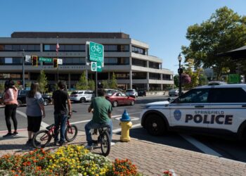 People watch as Springfield Police Department officers investigate the Springfield City Hall after bomb threats were made against buildings earlier in the day in Springfield, Ohio on September 12, 2024. - A government building and school were evacuated after an alleged bomb threat Thursday in Springfield, Ohio, local media reported, rattling the small city at the heart of an anti-migrant conspiracy theory amplified by Donald Trump. Springfield has been thrust into the spotlight in recent days after an unfounded story of Haitian migrants eating pets went viral on social media, with the Republican ex-president and current White House candidate pushing the narrative despite it being debunked. (Photo by ROBERTO SCHMIDT / AFP)