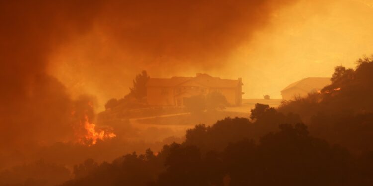 Smoke and flames engulf a hillside near homes (R) during the Airport Fire near Lake Elsinore, California, on September 10, 2024. - Out-of-control wildfires surrounding Los Angeles continued to grow on September 10, forcing families to evacuate and blanketing the sky with choking smoke. The fast-moving Airport Fire in Orange County has consumed more than 9,000 acres (3,600 hectares) since it was started accidentally on Monday afternoon by workers operating heavy equipment. (Photo by David SWANSON / AFP)