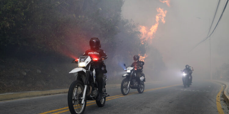 AME2229. QUITO (ECUADOR), 24/09/2024.- Policías patrullan en moto cerca a un incendio forestal este martes, Guapulo, Quito (Ecuador). Varios incendios forestales en los alrededores de Quito, la capital de Ecuador, han teñido con una espesa capa de humo a la ciudad, por lo que la autoridades han lanzado una alerta por la mala calidad del aire, sobre todo en el norte de la ciudad. EFE/ Santiago Fernández