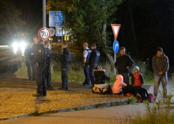 La policía federal alemana aguarda junto a varios refugiados que esperan en la frontera entre Freilassing, Alemania, y Salzburgo, Austria, el lunes 14 de septiembre de 2015. Alemania reintrodujo los controles temporales de frontera el domingo para reducir el ritmo de llegada de los miles de refugiados que cruzan su frontera, enviando un claro mensaje a sus socios europeos de que necesita más ayuda para lidiar con la crisis. (AP Foto/Kerstin Joensson)