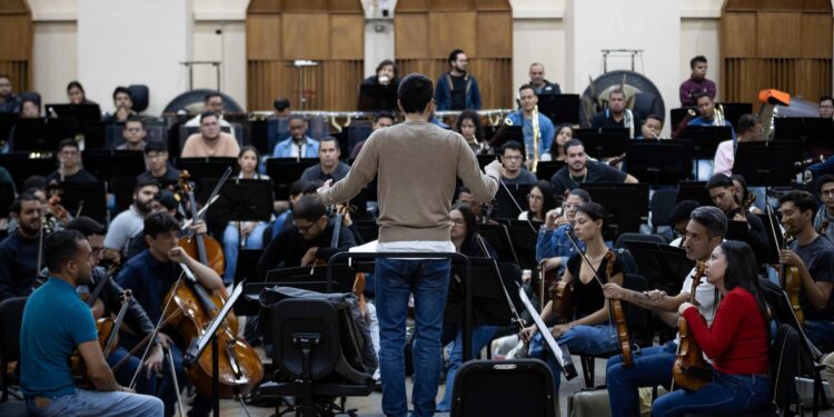 AME7375. CARACAS (VENEZUELA), 26/12/2024.- Fotografía del 17 de diciembre de 2024 del director académico musical Andrés David Ascanio Abreu (c), durante una práctica con la Orquesta Sinfónica Simón Bolívar de Venezuela en Caracas (Venezuela). El Sistema de Orquestas y Coros Juveniles e Infantiles de Venezuela celebrará el 50 aniversario de su fundación una gira por Europa de la mano del maestro Gustavo Dudamel, que incluirá encuentros académicos con niños y jóvenes, así como conciertos conjuntos en siete ciudades, dijo en una entrevista con EFE Eduardo Méndez, director ejecutivo de la agrupación musical. EFE/ Ronald Peña R.