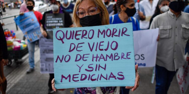 An opposition demonstrator holds a sign reading “I want to die at an old age not from hunger and without medicines” during a protest against the lack of electricity, medicines, water, the poor conditions of hospitals, and in demand of fairer salaries, in Caracas on April 14, 2022. (Photo by Federico PARRA / AFP)