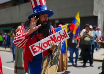 ARCHIVO - Un hombre vestido como el personaje estadounidense Tío Sam sostiene un cartel de la petrolera Exxon durante una marcha por el Esequibo, en Caracas, Venezuela, el 26 de septiembre de 2023.