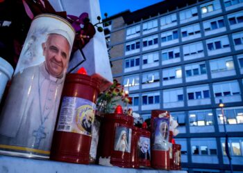 Rome (Italy), 22/02/2025.- A candle with the image of Pope Francis (L) sits at the foot of the statue of Pope St. John Paul II outside Gemelli University Hospital, where Pope Francis is battling pneumonia and a respiratory infection, in Rome, Italy, 22 February 2025. Pope Francis was hospitalized on 14 February due to a respiratory tract infection. (Papa, Italia, Roma) EFE/EPA/GIUSEPPE LAMI