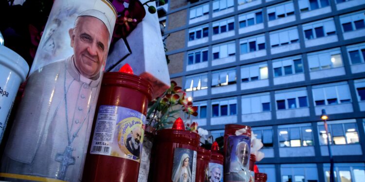 Rome (Italy), 22/02/2025.- A candle with the image of Pope Francis (L) sits at the foot of the statue of Pope St. John Paul II outside Gemelli University Hospital, where Pope Francis is battling pneumonia and a respiratory infection, in Rome, Italy, 22 February 2025. Pope Francis was hospitalized on 14 February due to a respiratory tract infection. (Papa, Italia, Roma) EFE/EPA/GIUSEPPE LAMI