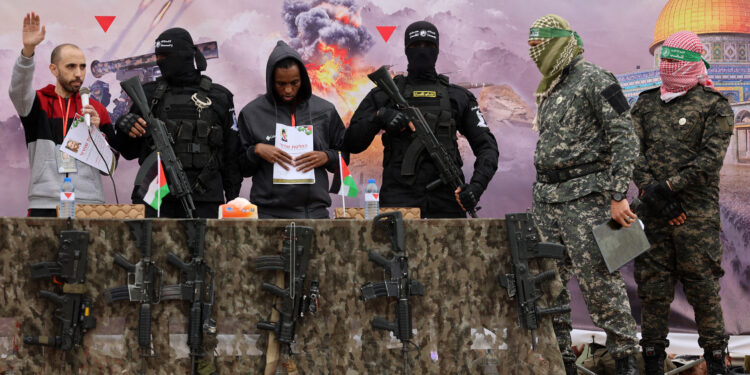 Israeli hostages Avera Mengistu (4th-R) and Tal Shoham (L) are flanked by Palestinian Hamas fighters as they stand on a stage during their release in Rafah in the southern Gaza Strip on February 22, 2025. Masked militants paraded Tal Shoham and Avera Mengistu on stage in the southern Gazan city of Rafah before handing them over to officials from the Red Cross. (Photo by Omar AL-QATTAA / AFP)